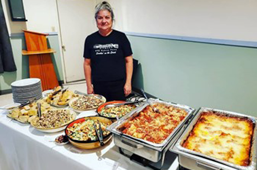 Patty behind catering table with lasagna, raviolis and much more